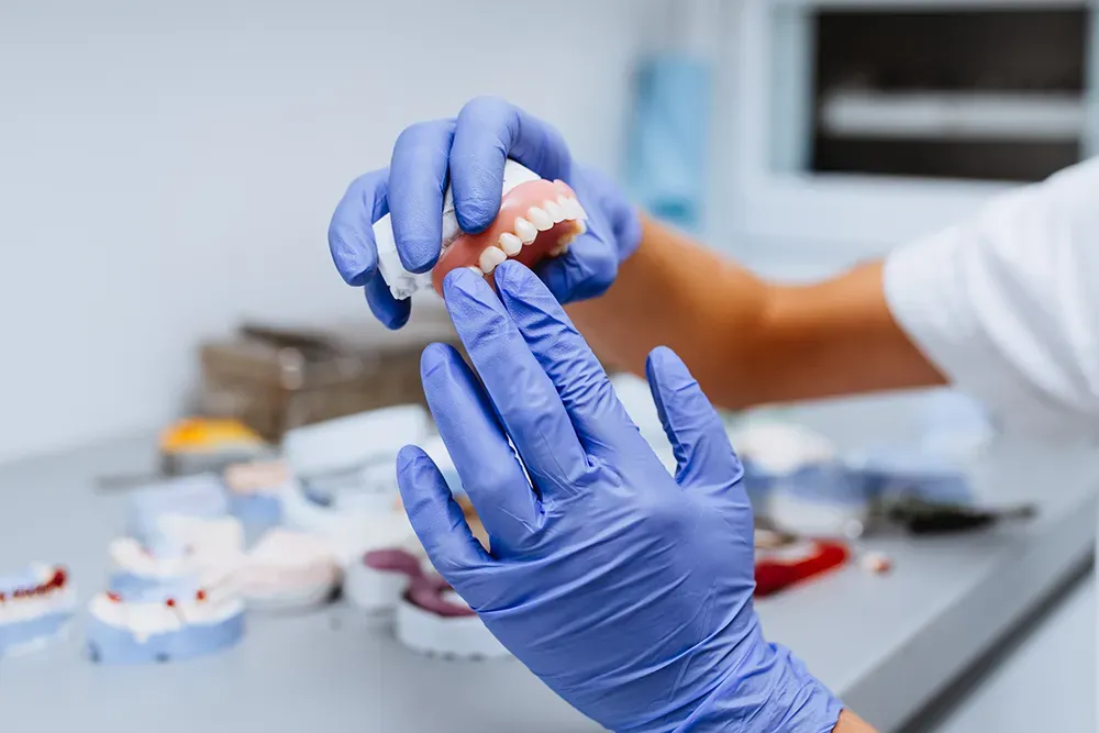 Dental technician in blue gloves holding a set of custom-made teeth in a dental lab