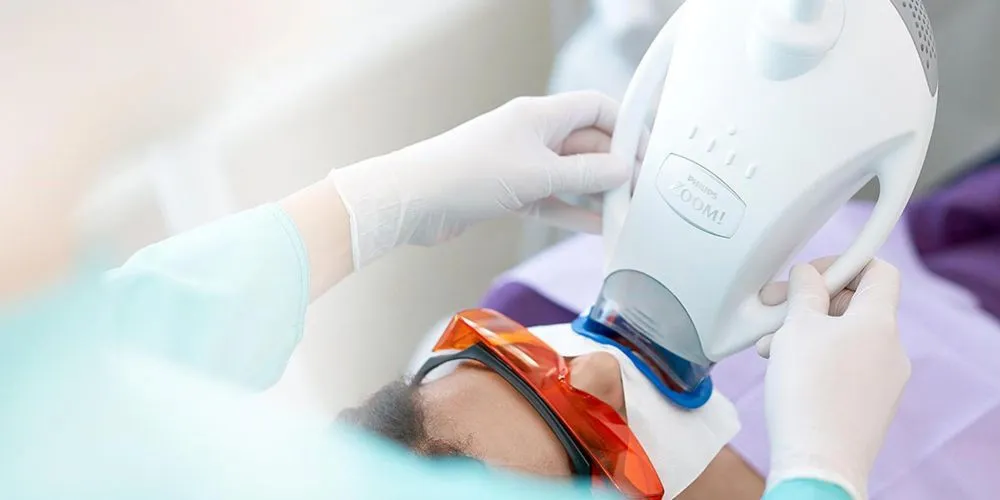 Patient wearing protective glasses during in-office Zoom teeth whitening with a blue LED light
